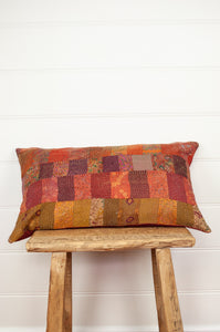 Vintage silk patchwork kantha bolster cushion in shades of orange, rose, burgundy, floral prints and highlights of lilac purple and olive green.
